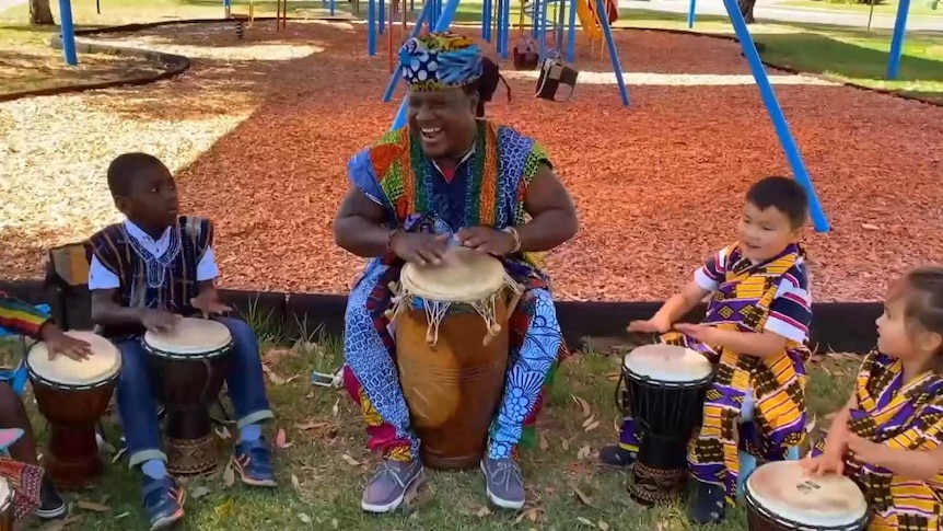 Teacher and students sit in a ring each with a bongo drum
