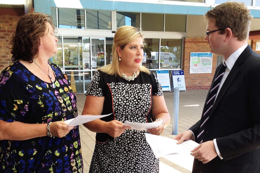 A woman with blonde hair speaking to a man and a woman