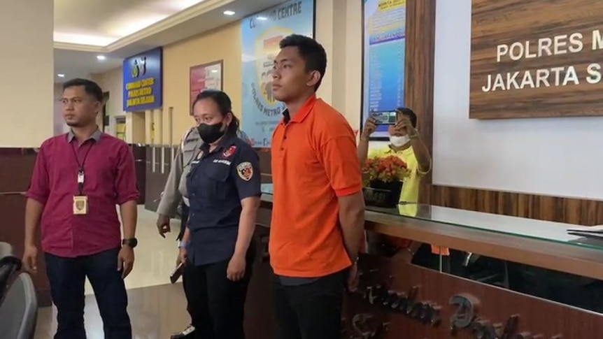 A photo of Mario Dandy Satrio under authorities arrest. He is wearing an orange shirt. 