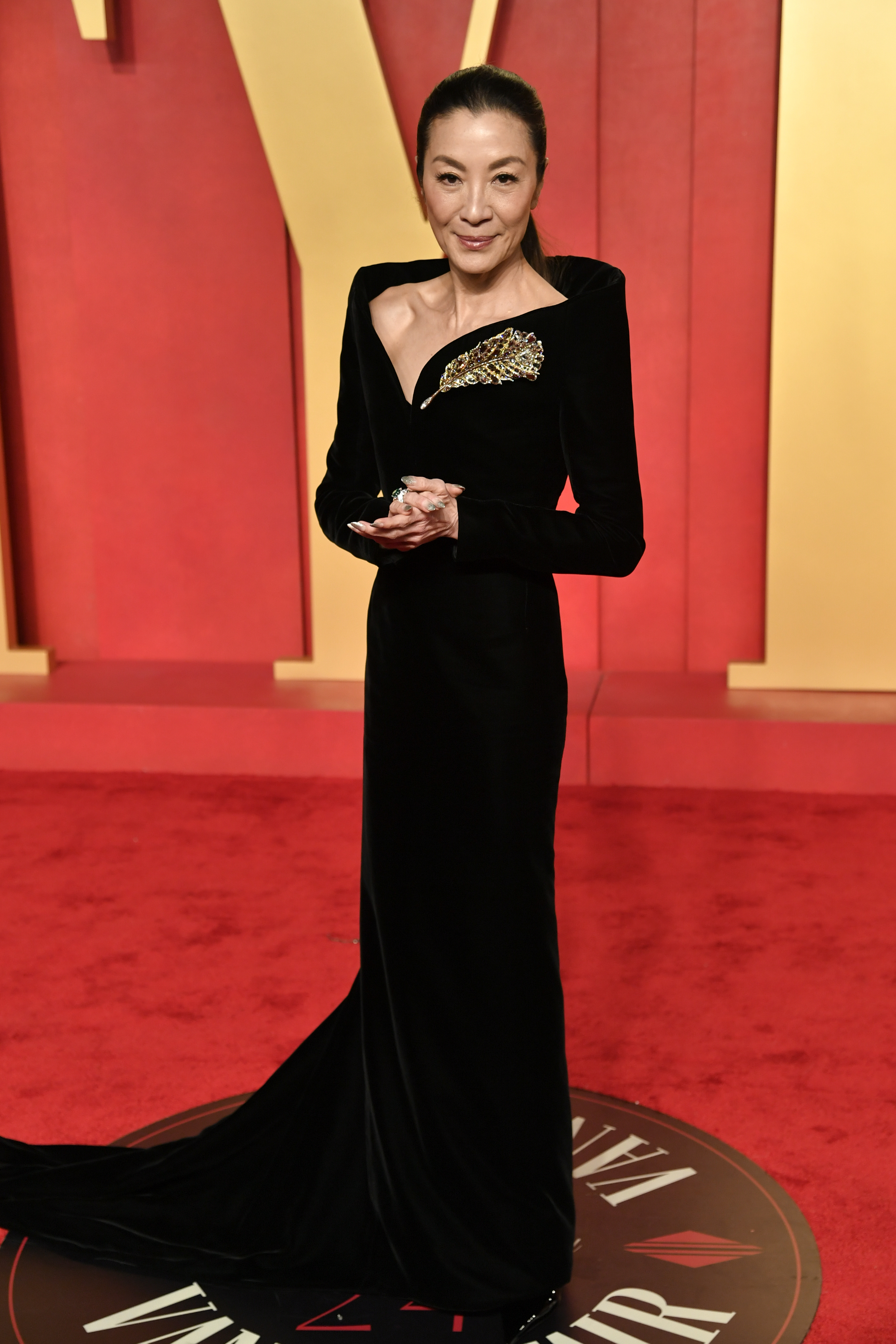 Michelle Yeoh wearing a long black gown with long sleeves, a structured neckline and a big sparkly gold feather brooch  