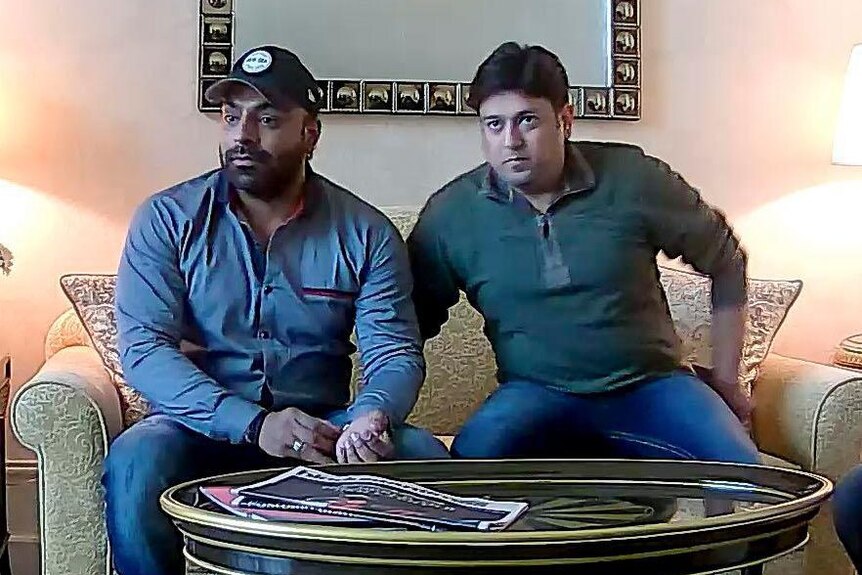 Two men are seen sitting on a couch.