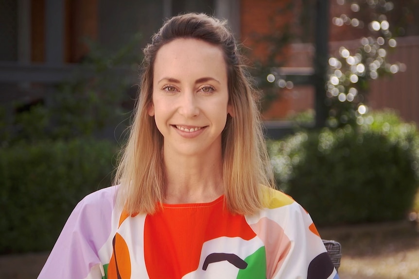 A woman, wearing a bright dress, smiles at the camera.