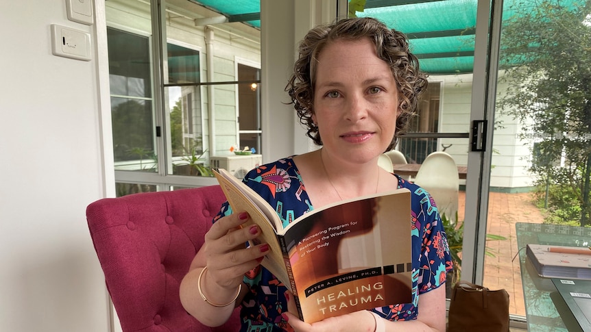 A woman holds an open book about healing trauma.