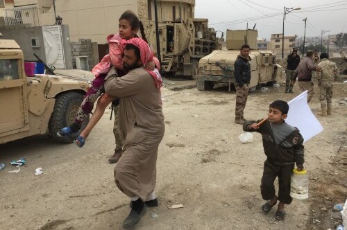 A man runs carrying his daughter on his shoulder, while a young boy carryies a white flag beside him.