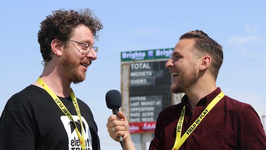 Tight shot of one man standing outside interviewing another with a microphone.