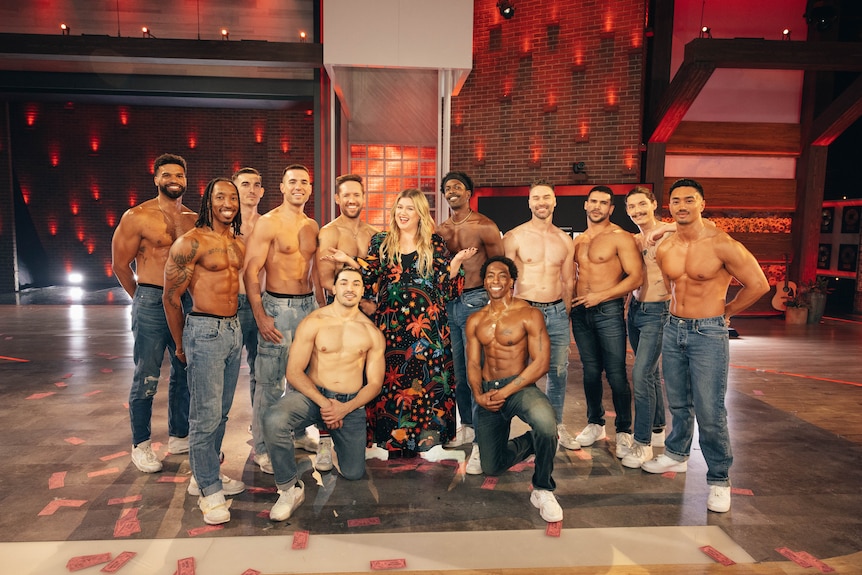 A group of shirtless men stand beside Kelly Clarkson