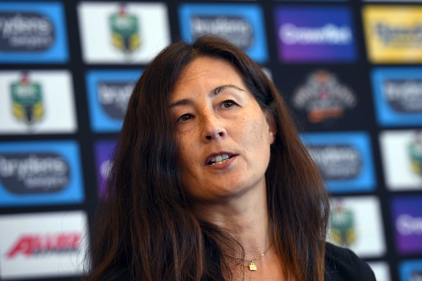 Marina Go speaks while sitting in front of an advertising board.