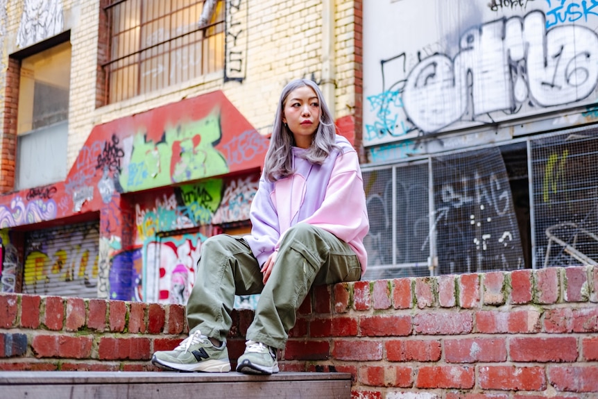 A photo of Li-Anne sitting on a brick wall staring into the distance.