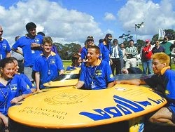 Team-members in blue shirts beside a bright yellow streamlined solar car