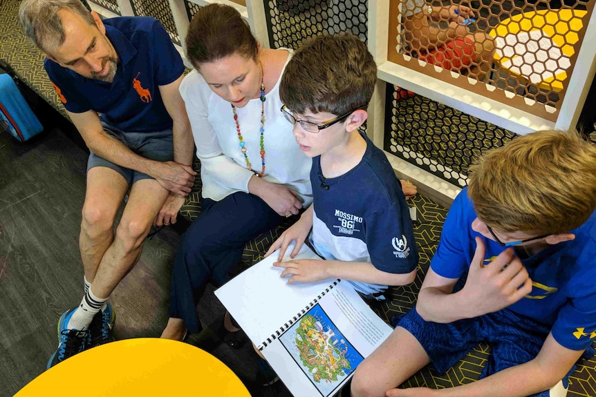 Father, mother, Josh and his brother Ben sitting as Josh reads a braille book.