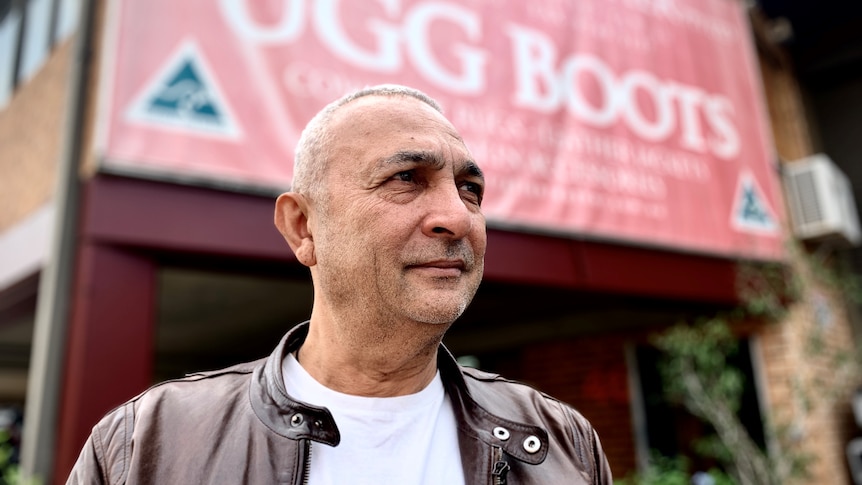 A man in leather jacket stands in front of a sign saying ugg boots.