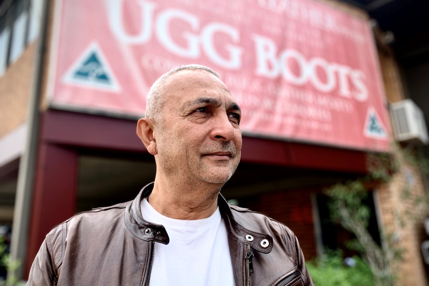 A man in leather jacket stands in front of a sign saying ugg boots.