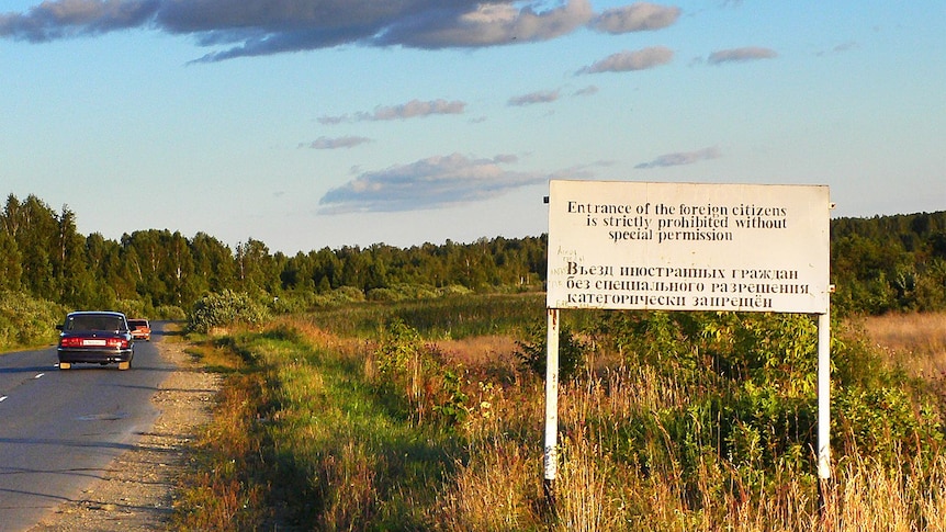 Looking across a bright green field with a road beside it, you view a sign telling people of restricted access to a road.