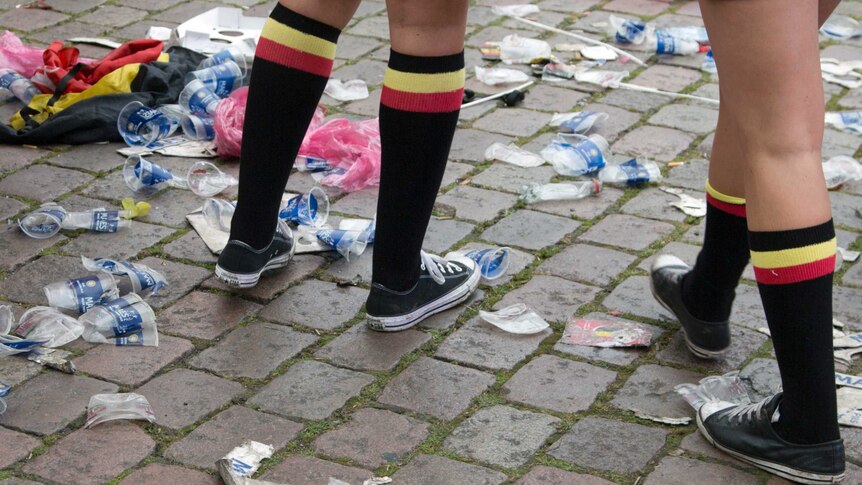 Belgian fans, wearing the Belgian colors, walk through plastic cups and other garbage