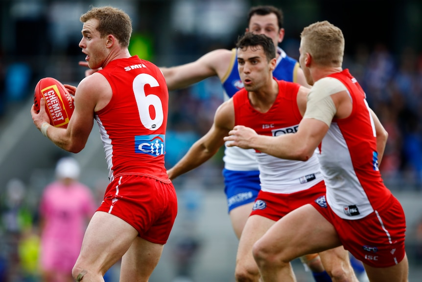 An AFL player holds the ball as he prepares to handball while surrounded by teammates.