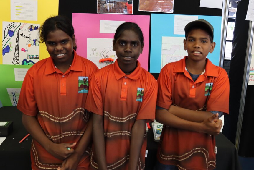Three Aboriginal kids in school uniforms stand in front of a science display