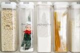 Christmas elf wearing a green hat and outfit in a clear jar on a shelf with jars of food around them 
