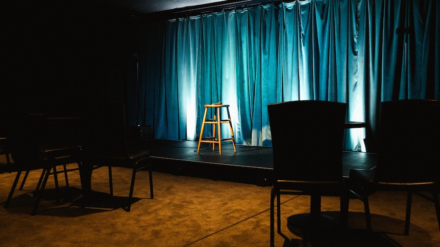 An empty room with a lit up blue curtain and stage with a vacated stool