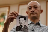 A Chinese man holds his father's portrait