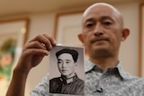 A Chinese man holds his father's portrait