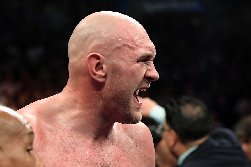 A shirtless Tyson Fury looks to the left with his mouth open and face scrunched up with sweat beading on his head.