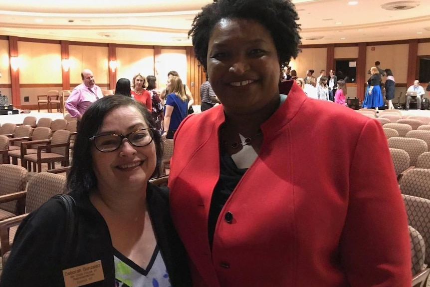 Stacey Abrams in a red jacket with her arm around a shorter woman wearing glasses