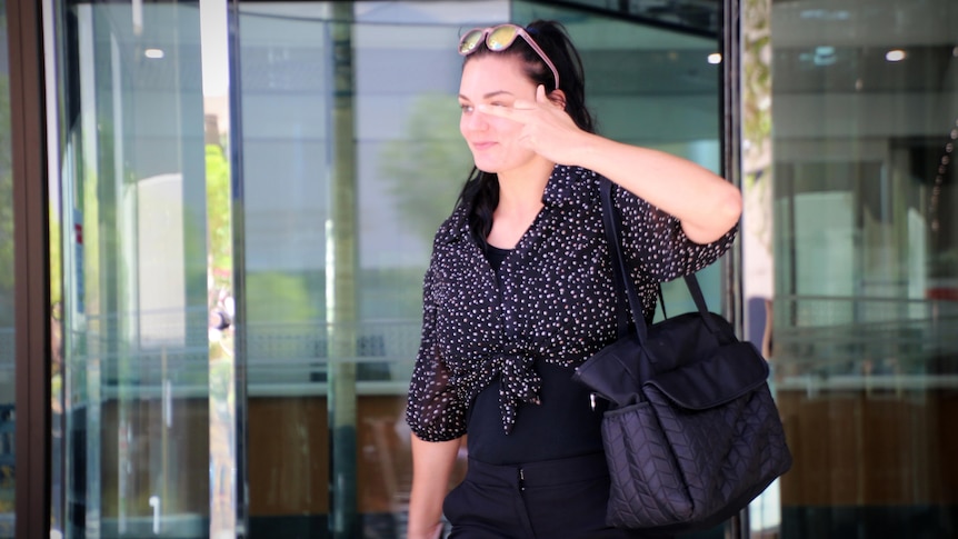 A woman in a black outfit walking out of court, showing her middle finger to the camera.