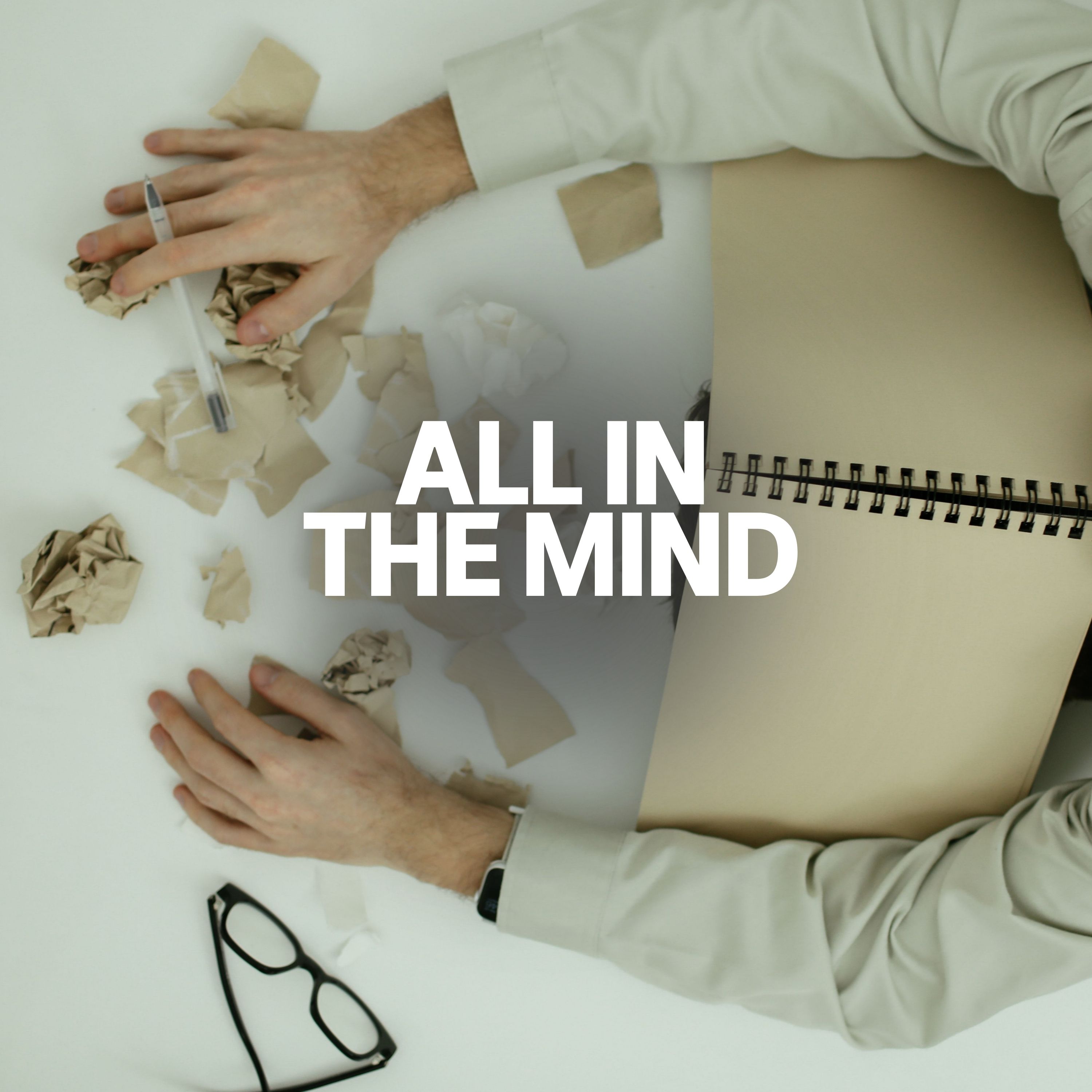 Someone with their head and hands on a cluttered desk, with a book over their head.