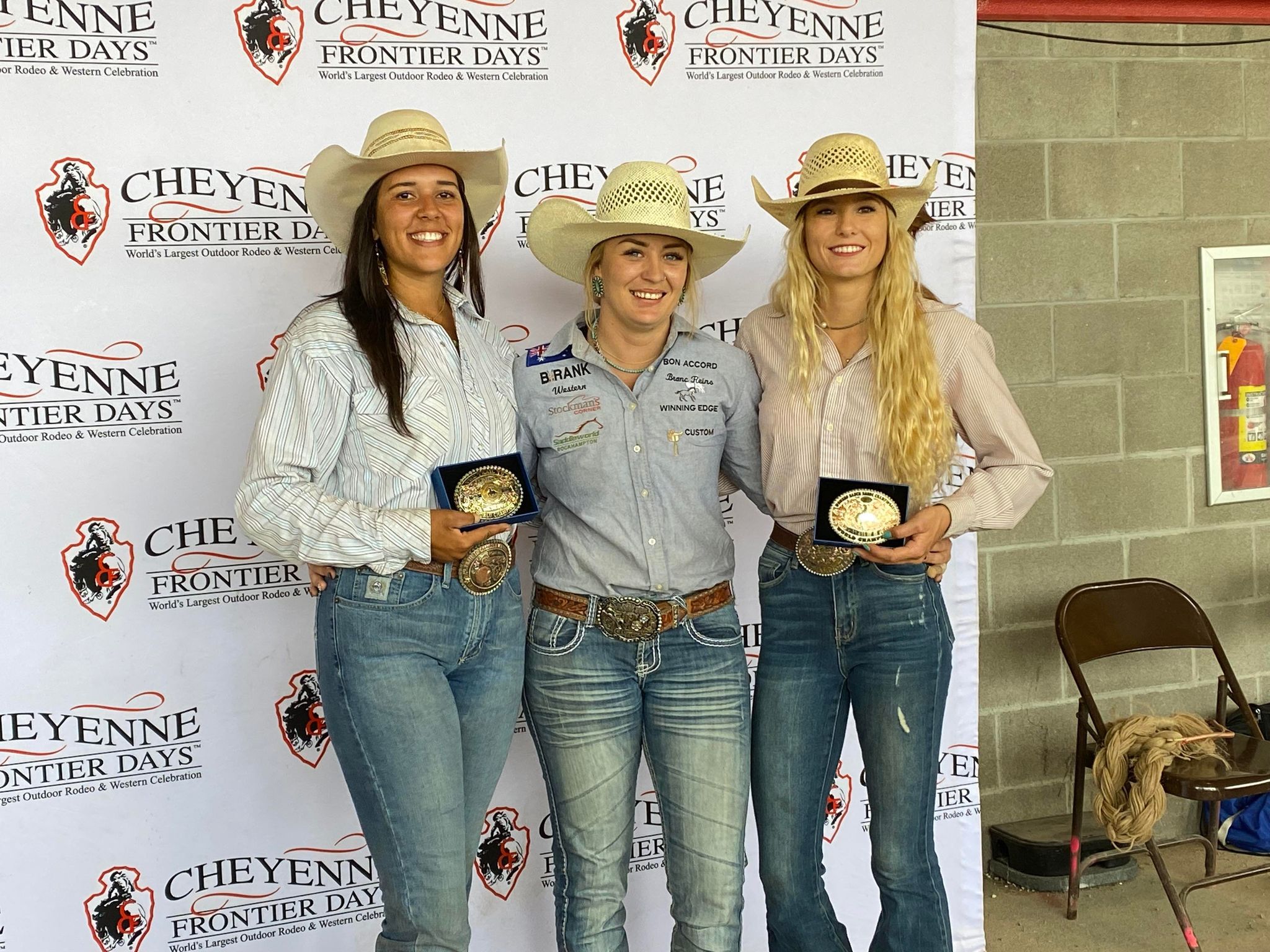 Three smiling women stand together in front of a sign that says "Cheyenne Frontier Days".