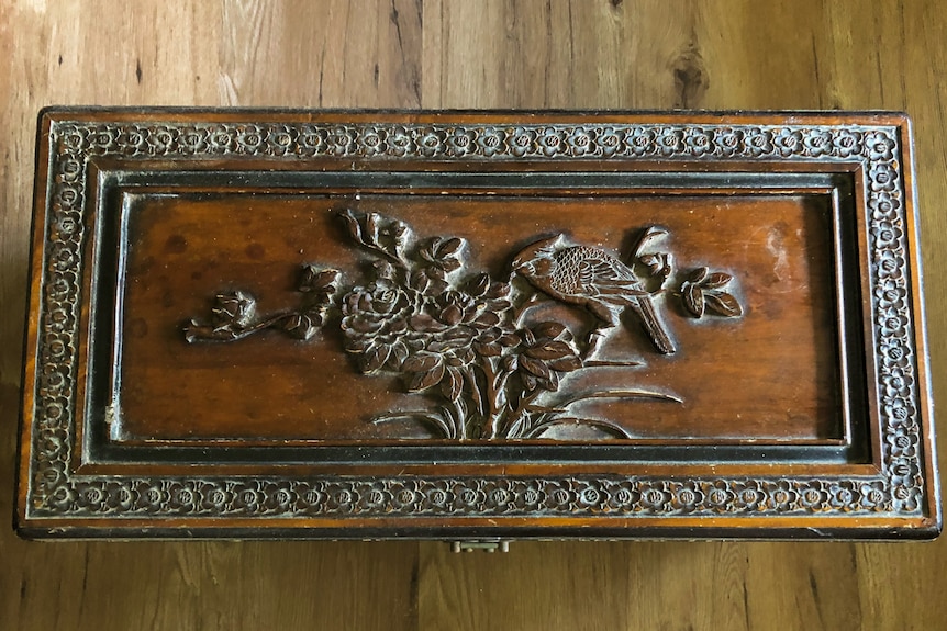 The lid of a wooden box carved with bird and a tree.