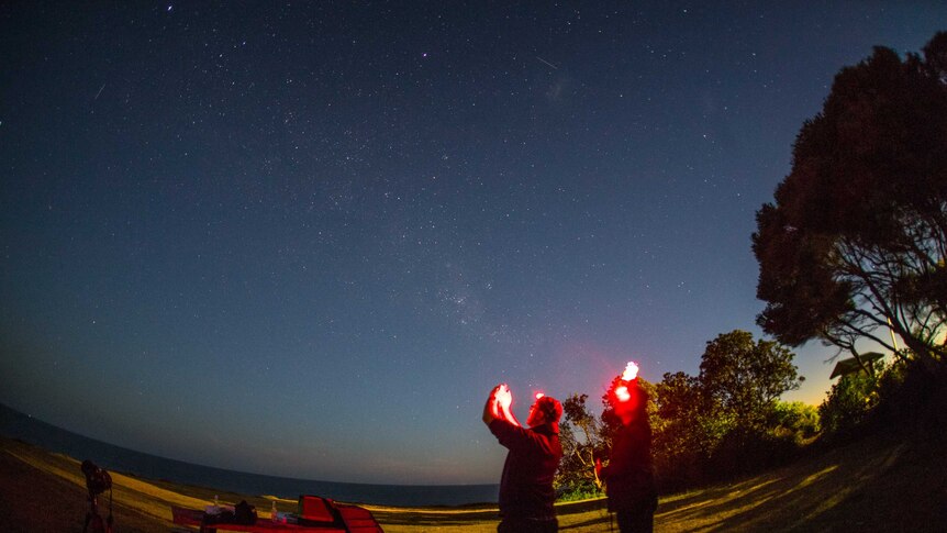 David Finlay and Chris Dengate hold their phones up to the sky at night time