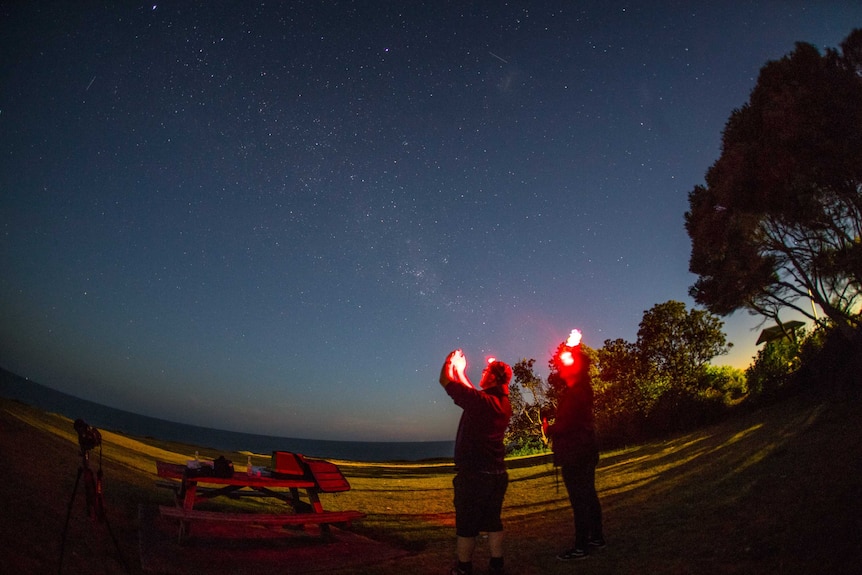 David Finlay and Chris Dengate hold their phones up to the sky at night time