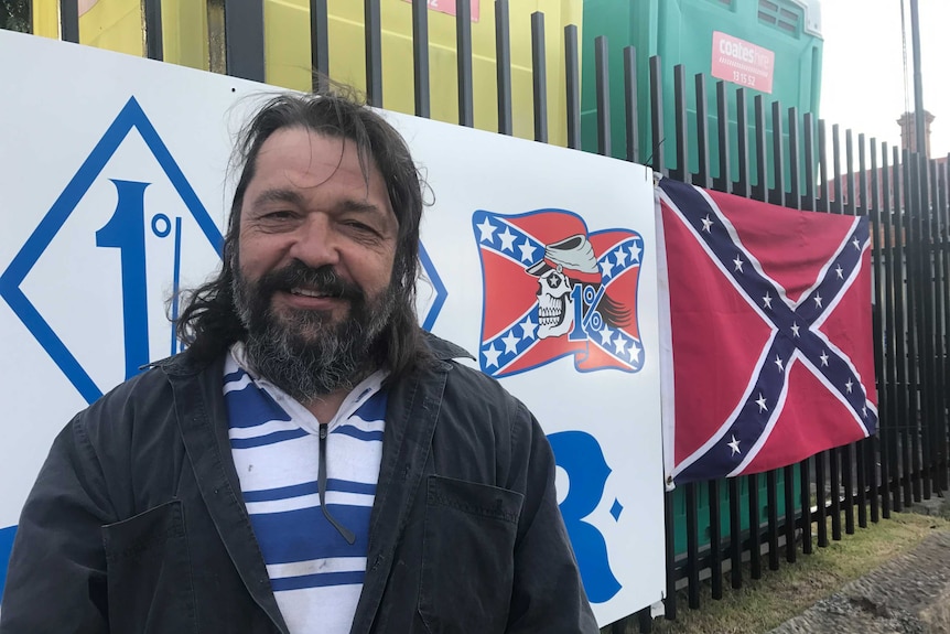 Rebels member Little Mick in front of club flags.