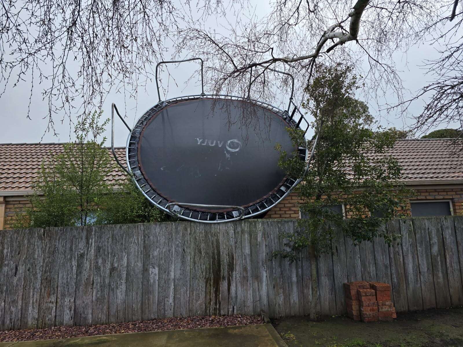 A large trampoline leaning on the side of a house after a being blown there by wind