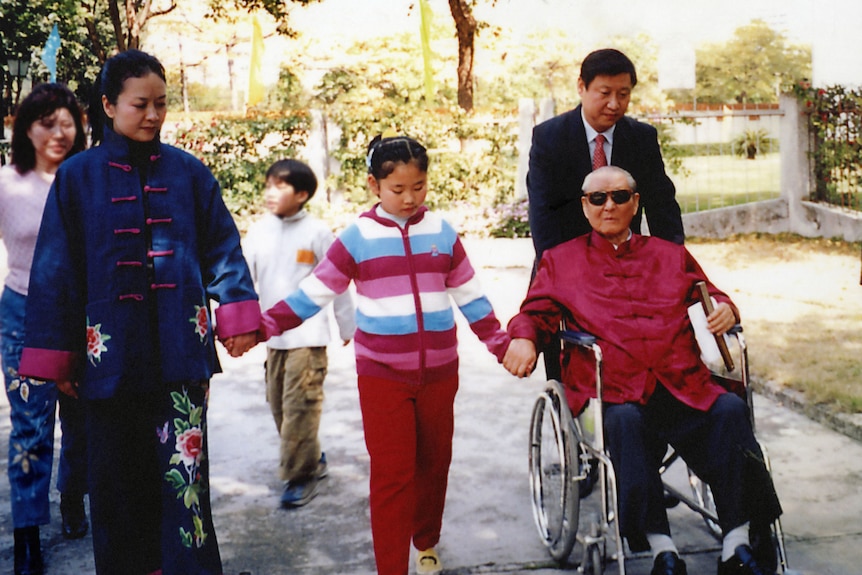 Xi Jinping pushes an older man, his father Xi Zhongxun, in a wheelchair. His family walk beside him