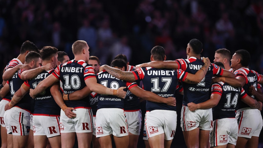 A group of Sydney Roosters NRL players stand in a circle wearing black armbands during a minute's silence.