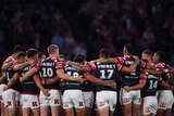 A group of Sydney Roosters NRL players stand in a circle wearing black armbands during a minute's silence.