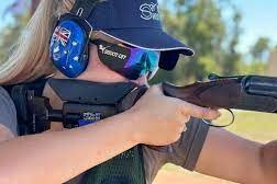 a girl with blonde hair and a blue cap shoots a shotgun 