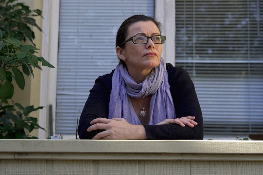 A woman stares off into the distance from her balcony