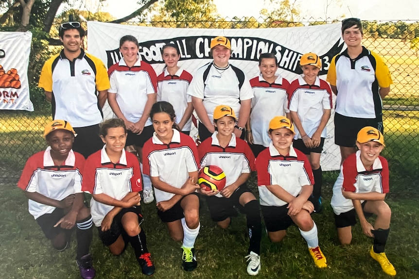 A girls soccer team smiles for a group photograph. A young Kyra Cooney-Cross is kneeling at the front holding a ball.