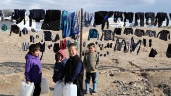 Boys stand holding water containers in a refugee camp.