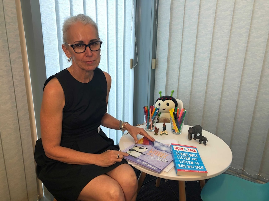 Woman sitting in low chair beside table with educational books.