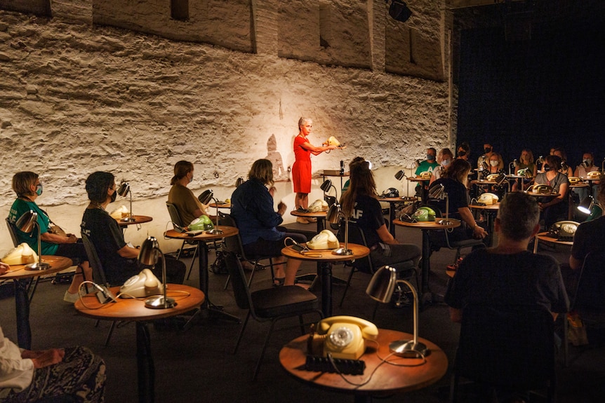 A dimly lit room with rows of small tables each with a lamp and rotary phone, and one person at each table.