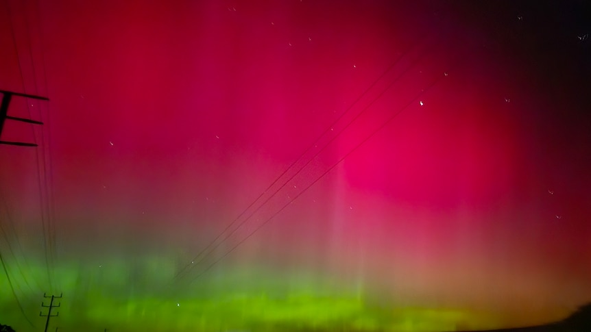 A night sky growing red and green with a silhouette of a telephone pole to the left of frame 