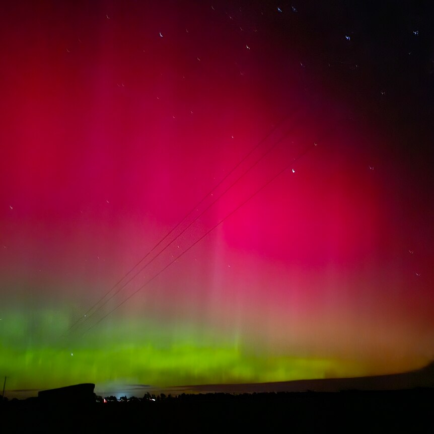 A night sky growing red and green with a silhouette of a telephone pole to the left of frame 