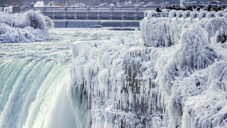 The brink of the Horseshoe Falls in Niagara Falls are stiff icicles and onlookers can be seen peering out over the falls.