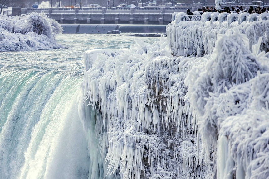 The brink of the Horseshoe Falls in Niagara Falls are stiff icicles and onlookers can be seen peering out over the falls.