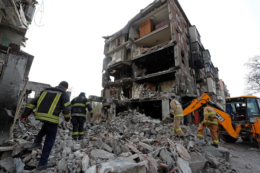 Los trabajadores atraviesan los escombros de un edificio de apartamentos destruido.