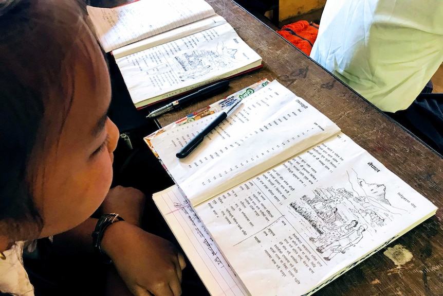 A young Nepalese girl works from a book at a school.