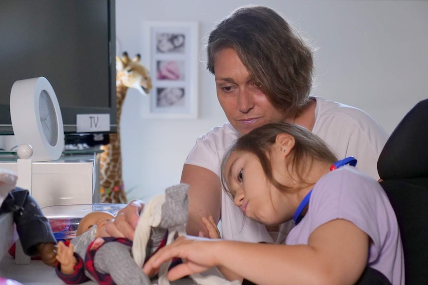 A photo of a mother playing with toys with her daughter, who uses a wheelchair.